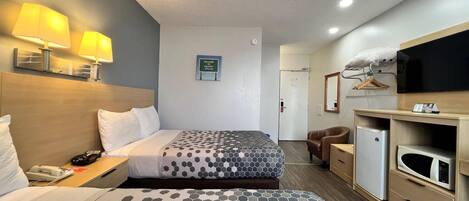 Habitación de hotel con dos camas, un escritorio con teléfono, televisión, microondas y refrigerador pequeño.