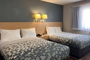 Une chambre d’hôtel avec deux lits, une table de chevet, une lampe et une fenêtre avec des rideaux.