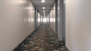 A long, narrow hallway with patterned carpet, white walls, and doors on both sides. - Econo Lodge Motel Village (Calgary)