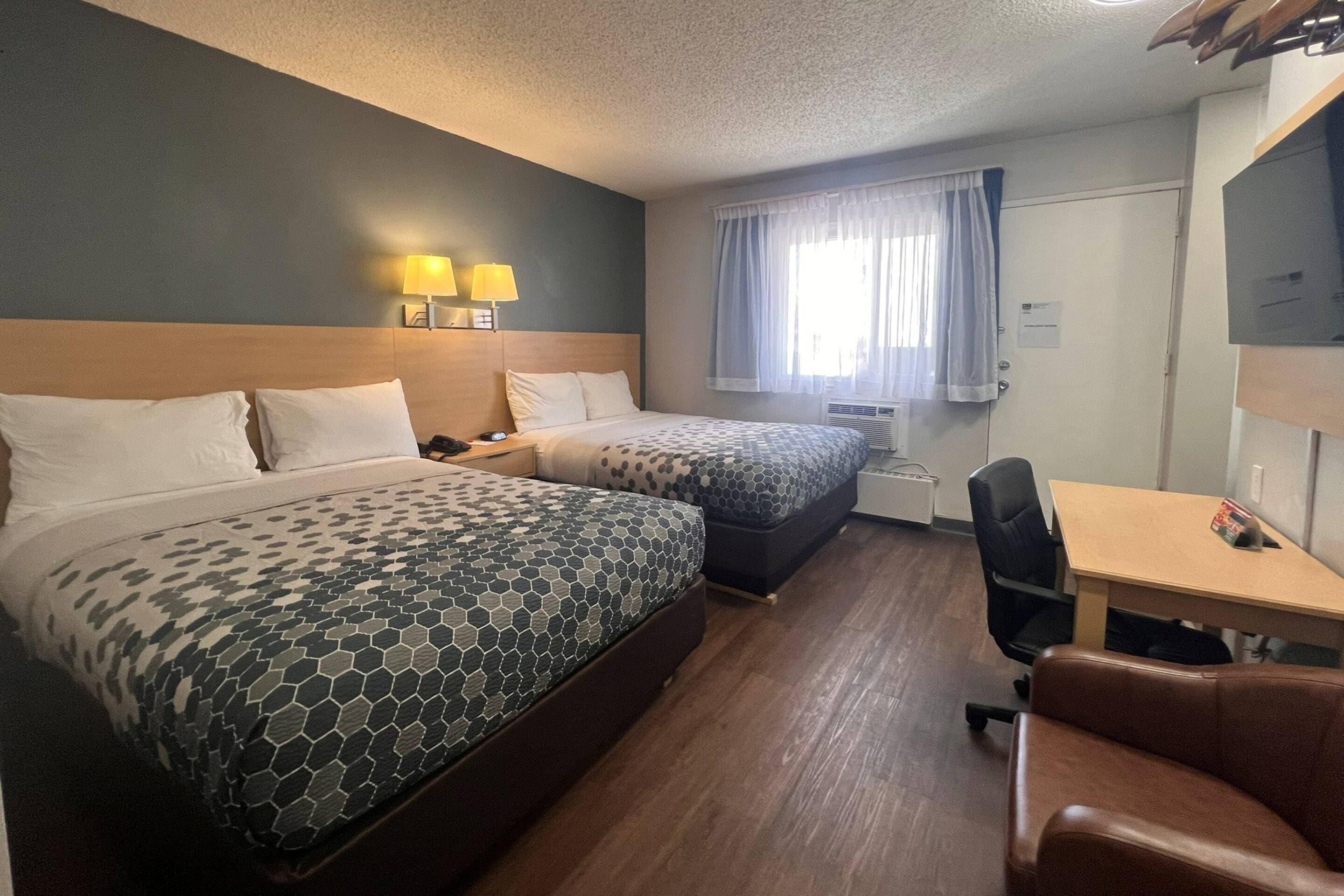 Hotelkamer met twee bedden, een bureau, een stoel, een raam met gordijnen en een tv aan de muur.