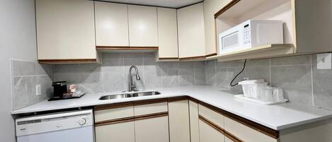 A compact kitchen with white cabinets, a stainless steel sink, a microwave, and a dishwasher.