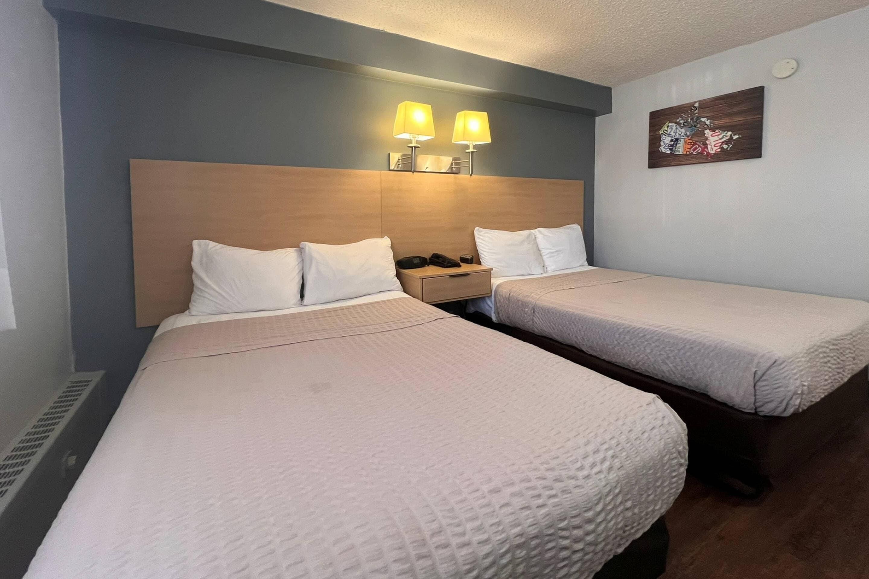 Habitación de hotel con dos camas, cabeceros, lámparas de noche y un cuadro colgado en la pared.
