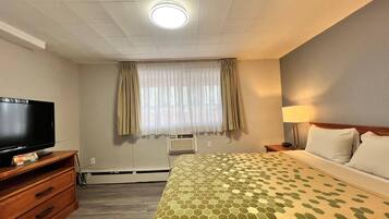 Habitación de hotel con televisión de pantalla plana, cama con colcha estampada, lámpara de noche y ventana con cortinas.