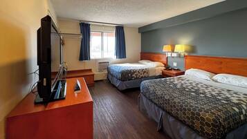 A hotel room with two beds, a desk with a television, a window with curtains, and a lamp on the nightstand.