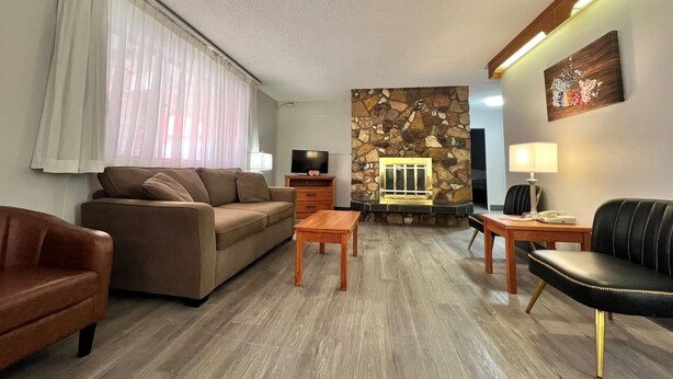 A living room with a stone fireplace, a sofa, a coffee table, and a TV. - Econo Lodge Motel Village (Calgary)