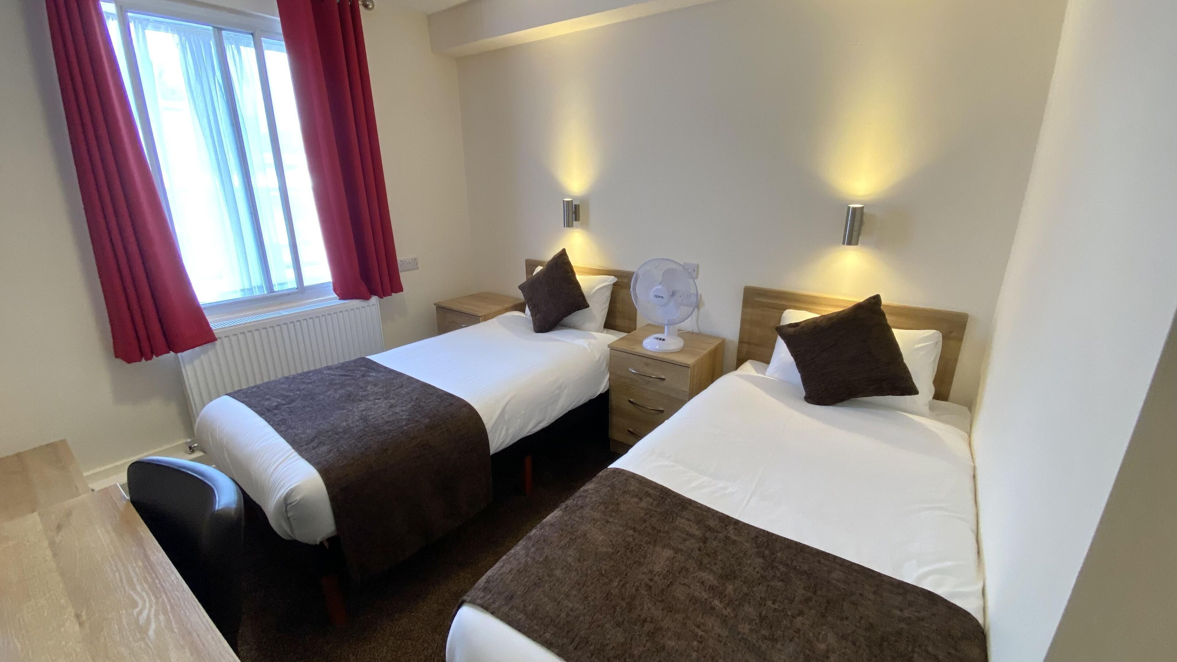 Une chambre d’hôtel avec deux lits simples, une table de chevet en bois, un bureau et une chaise.