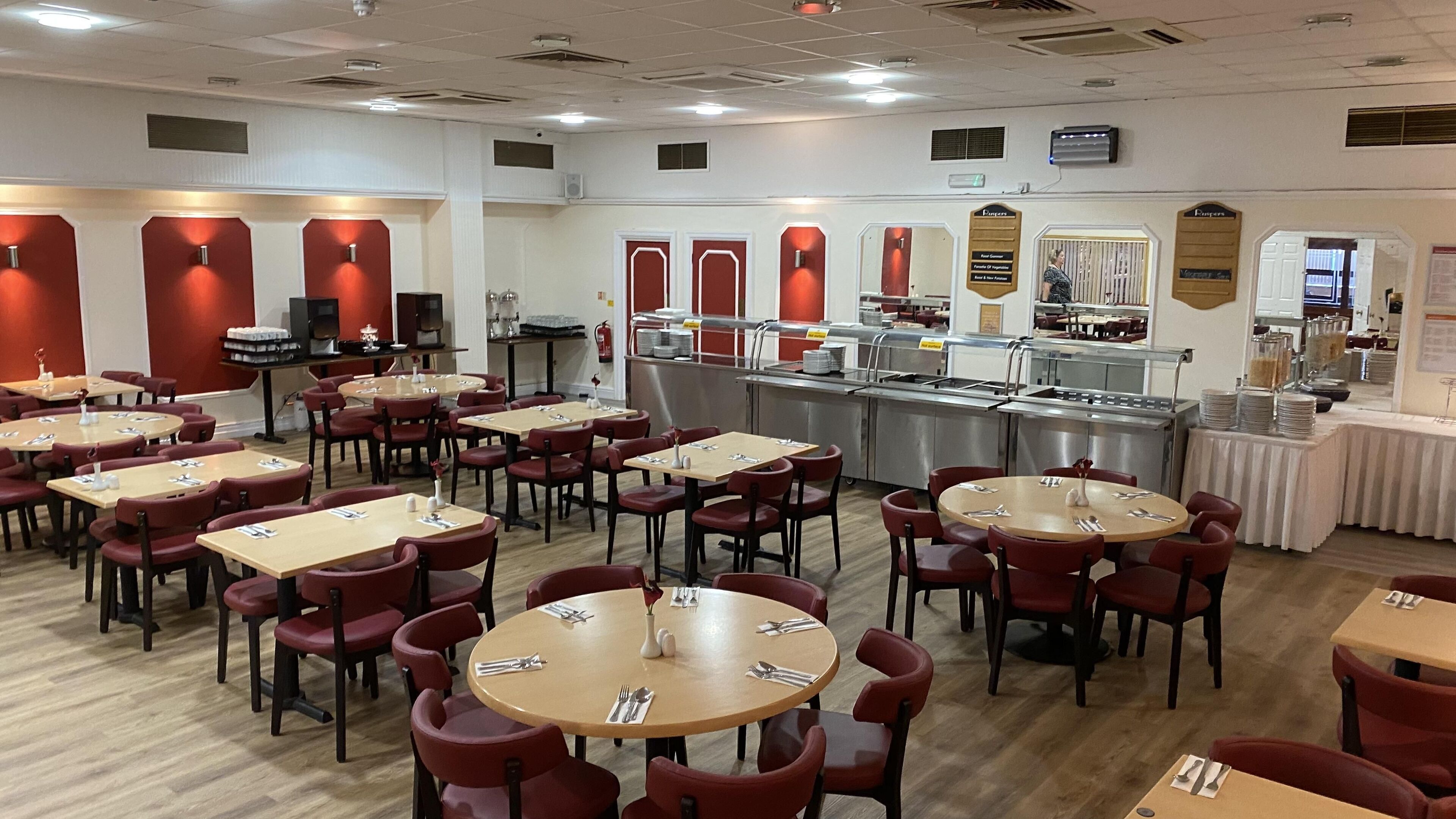 Un comedor con mesas redondas y sillas rojas, una barra de buffet y un menú en una pizarra colgada en la pared.