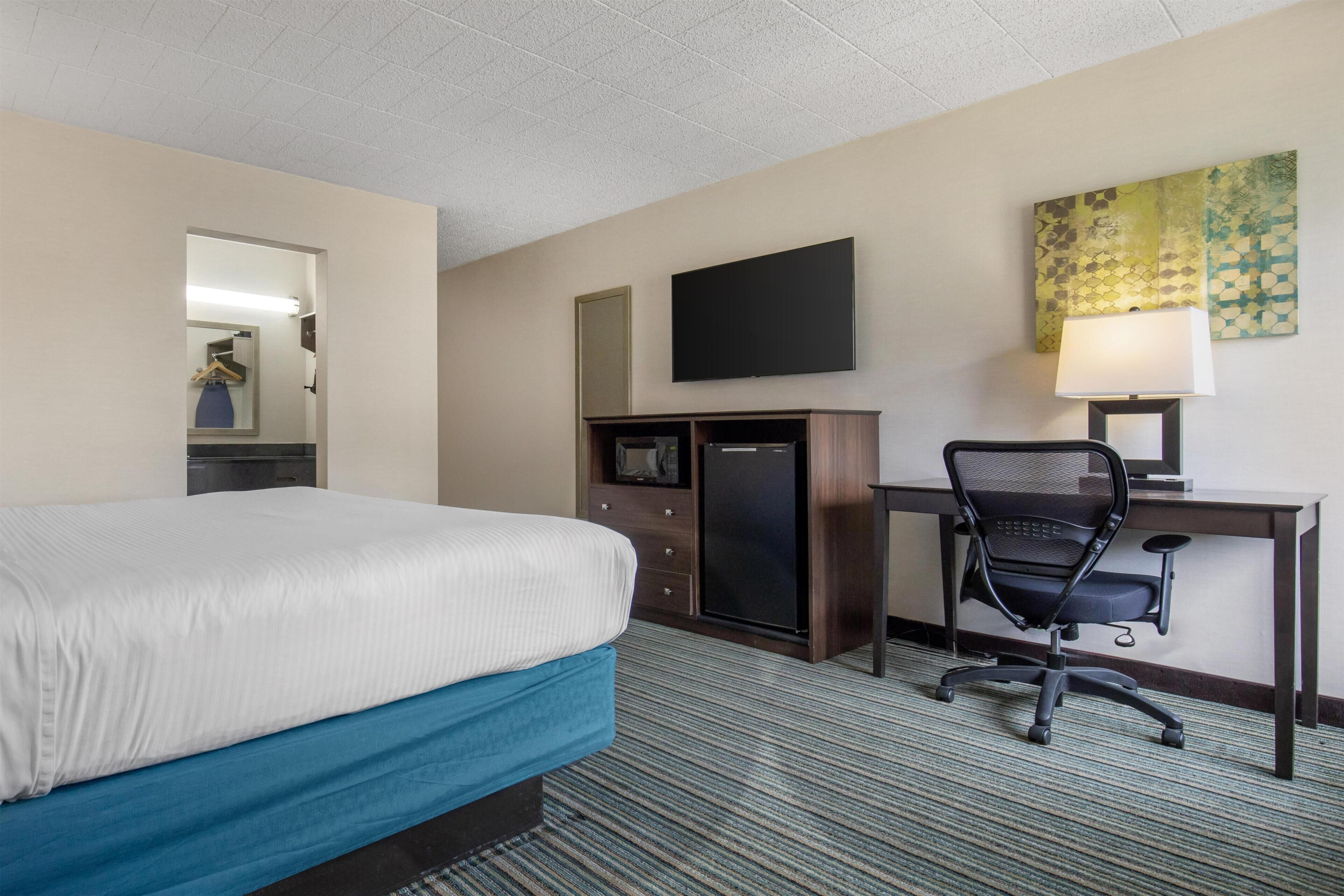 Une chambre d’hôtel équipée d’un lit, d’un bureau, d’une chaise, d’une télévision, d’un réfrigérateur et d’une lampe.
