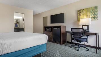 A hotel room with a bed, a desk, a chair, a TV, a refrigerator, and a lamp.