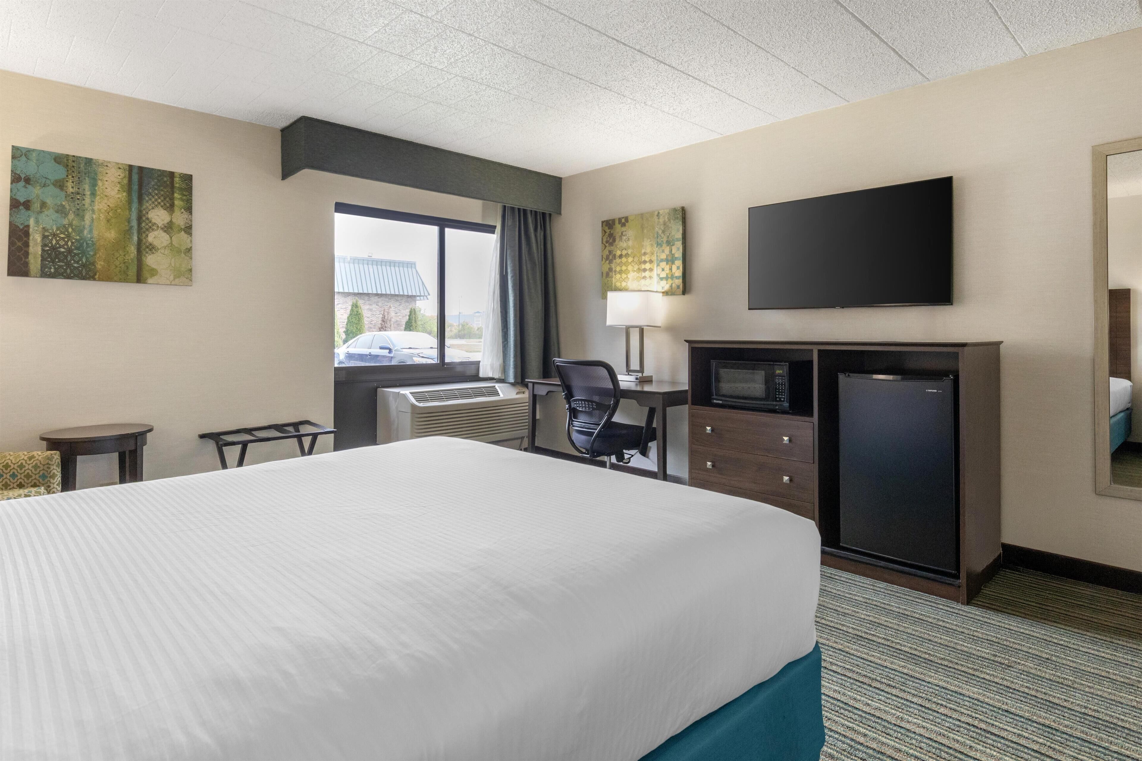 A hotel room with a large bed, a desk with a computer, a television, and a small refrigerator.