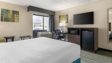A hotel room with a large bed, a desk with a computer, a television, and a small refrigerator.