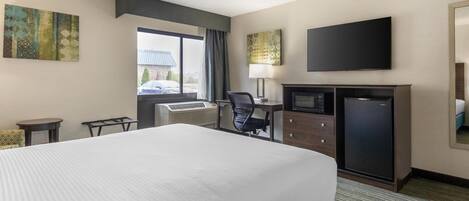 A hotel room with a large bed, a desk with a computer, a television, and a small refrigerator.