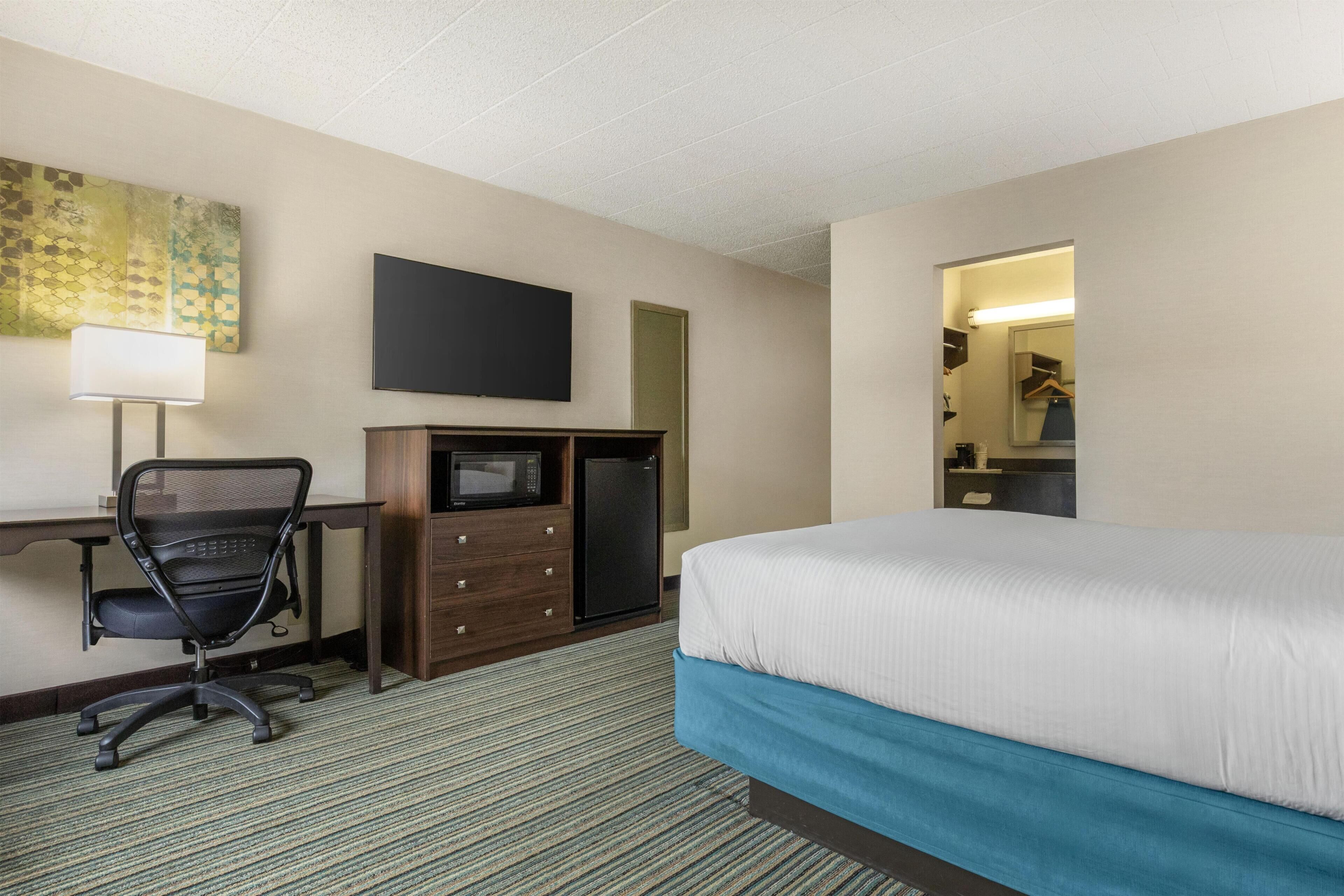 Habitación de hotel con cama, escritorio, silla, microondas y espejo.