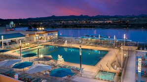 A hotel pool area with multiple pools, sun loungers, umbrellas, and a view of the surrounding landscape. - The Aquarius Casino Resort, BW Premier Collection (Laughlin)
