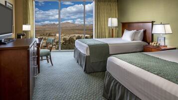 A hotel room with two beds, a desk, a chair, and a view of mountains.