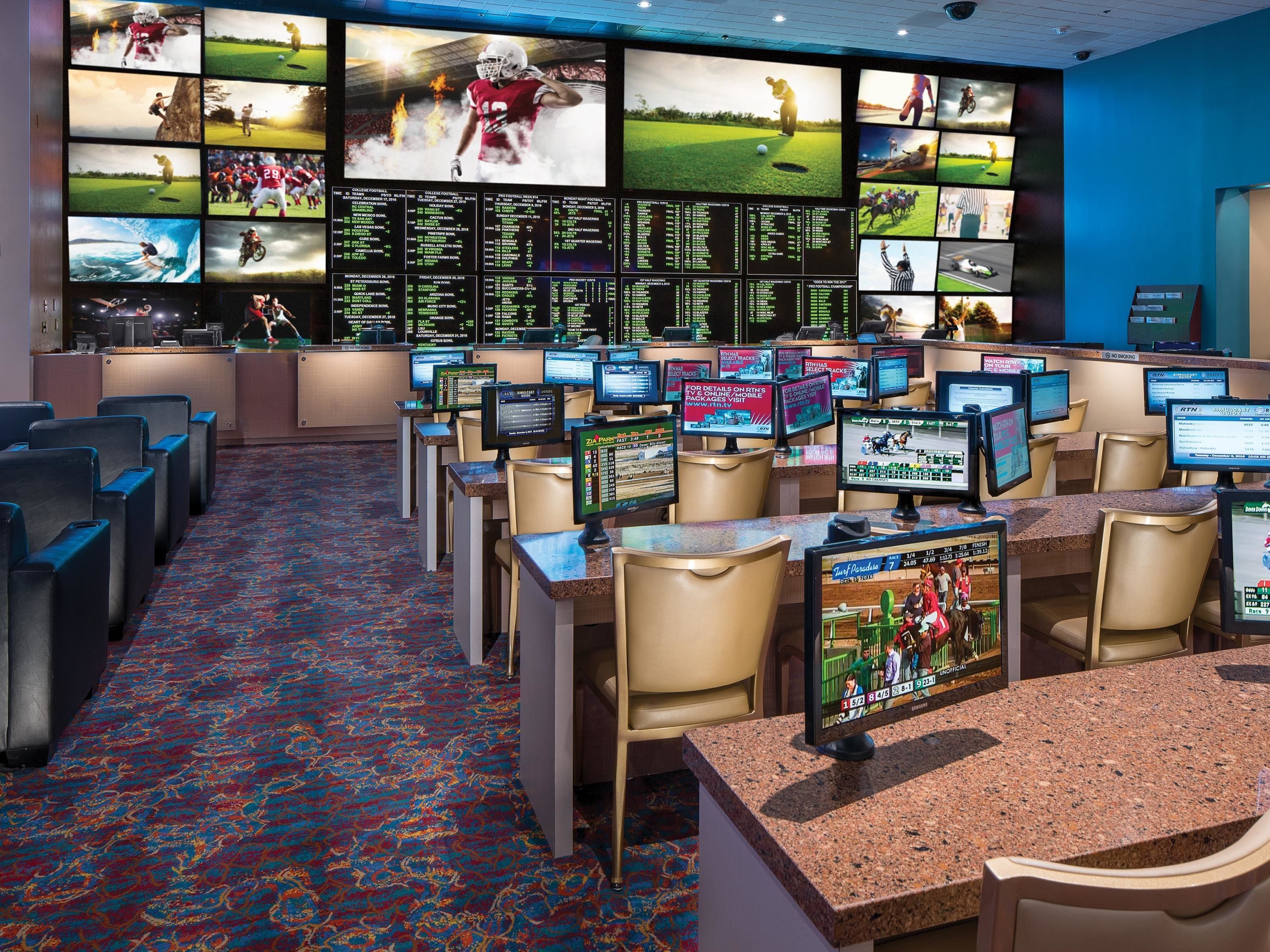 A sports betting area with multiple screens displaying various sports events, a carpeted floor, and seating arrangements.