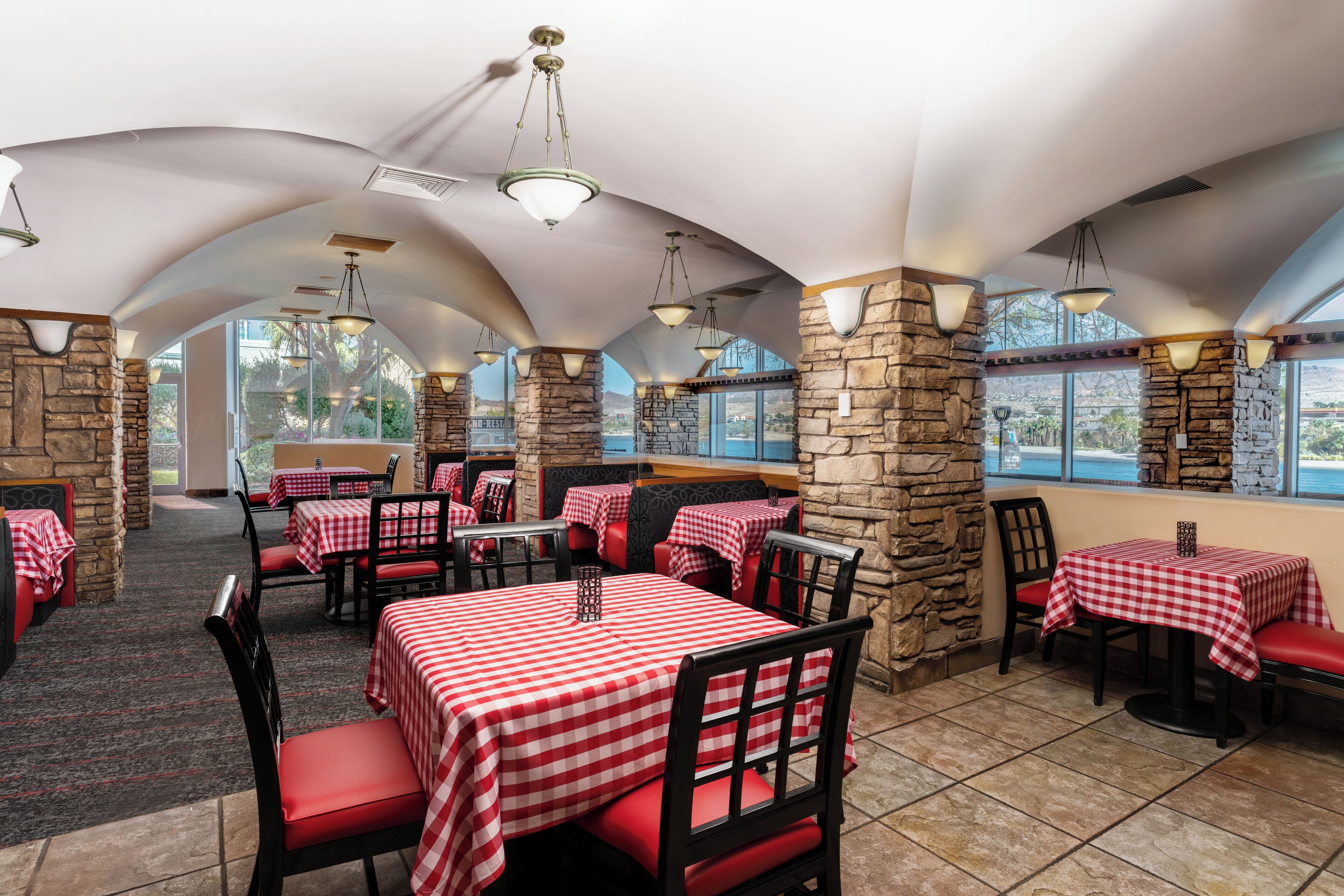 Un restaurant avec des nappes à carreaux, des piliers en pierre et des chaises rouges.