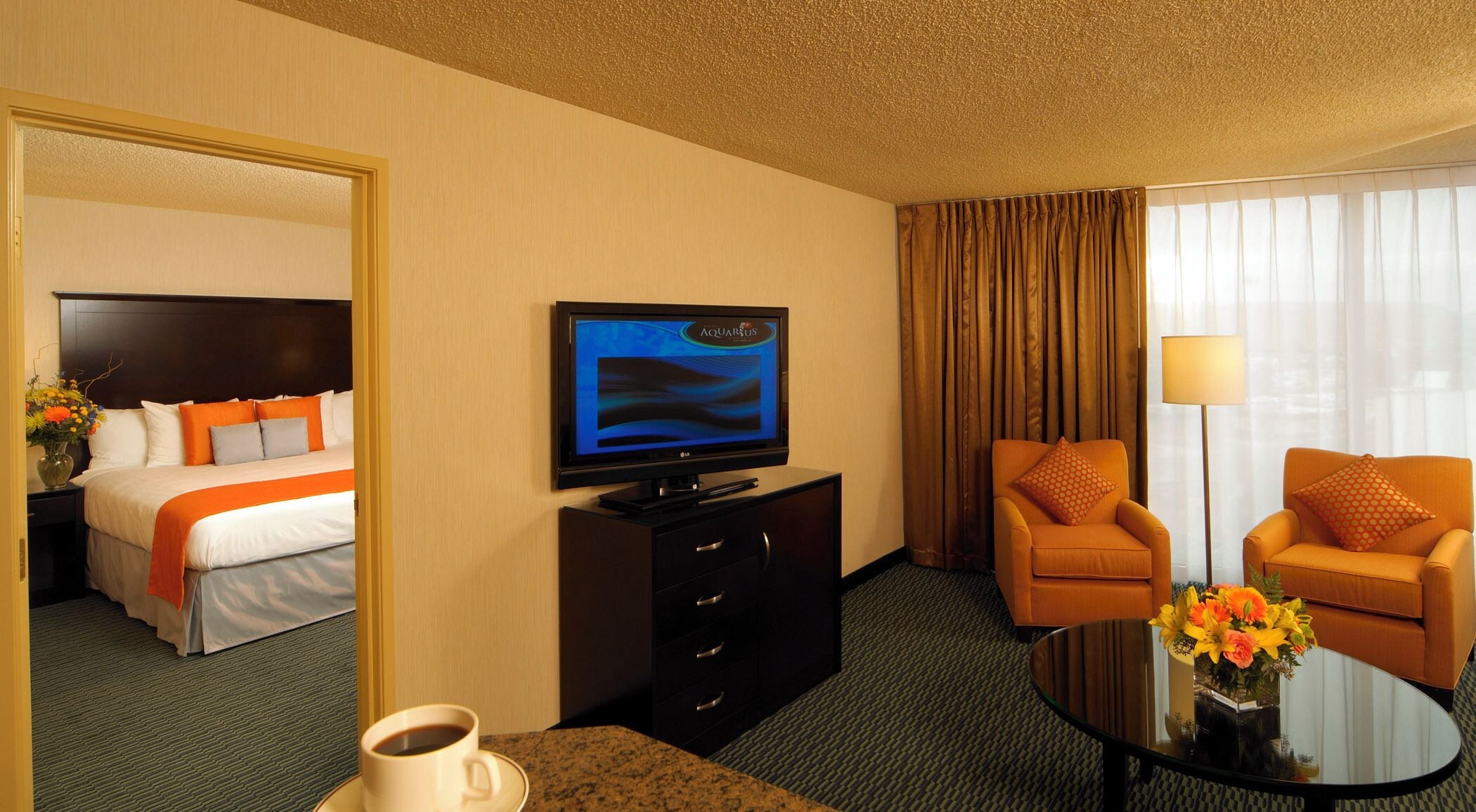 A hotel room with a bed, a television, a coffee table, and two armchairs.