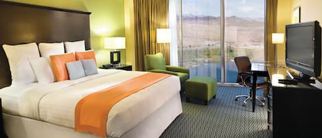 A hotel room with a large bed, a desk with a computer, a television, and a view of the desert through the window.