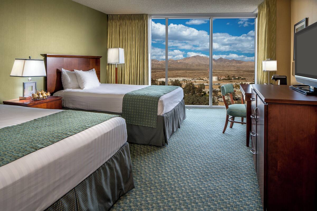 Ein Hotelzimmer mit zwei Betten, einem Schreibtisch, einem Stuhl und einem großen Fenster mit Blick auf die Berge.