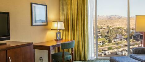 A hotel room with a bed, a desk, a chair, a television, and a window with a view of a desert landscape.