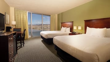 A hotel room with two beds, a desk with a computer, a TV, and a view of a mountainous landscape.