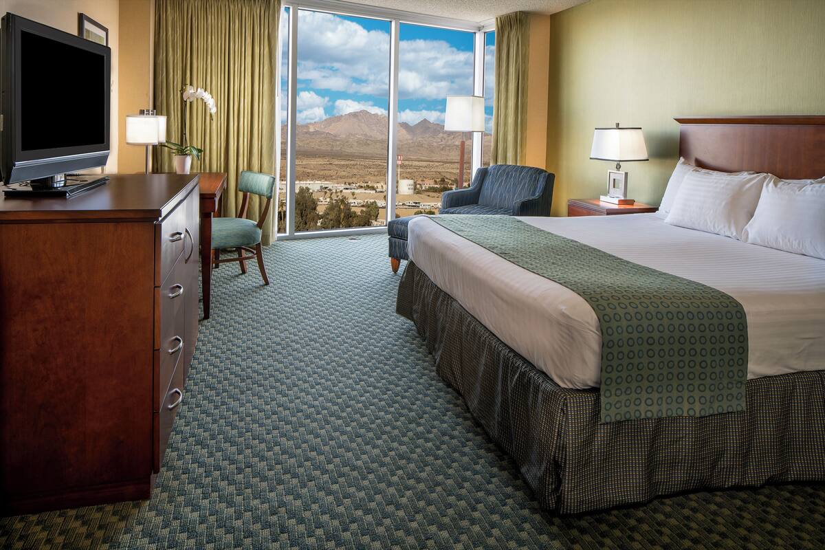 Ein Hotelzimmer mit einem großen Bett, einem Schreibtisch mit Fernseher, einem Sessel und Bergblick aus dem Fenster.