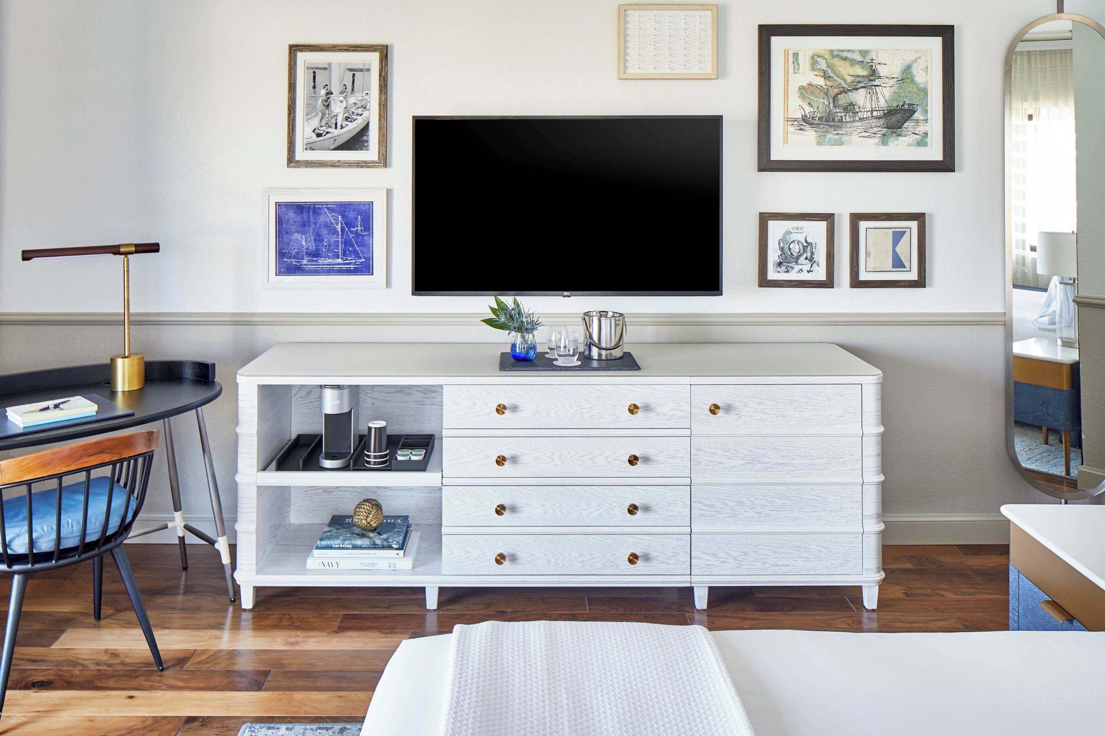 Une chambre moderne dotée d’un grand téléviseur à écran plat, d’une commode blanche avec de nombreux tiroirs, d’une petite table d’appoint et d’une chaise.