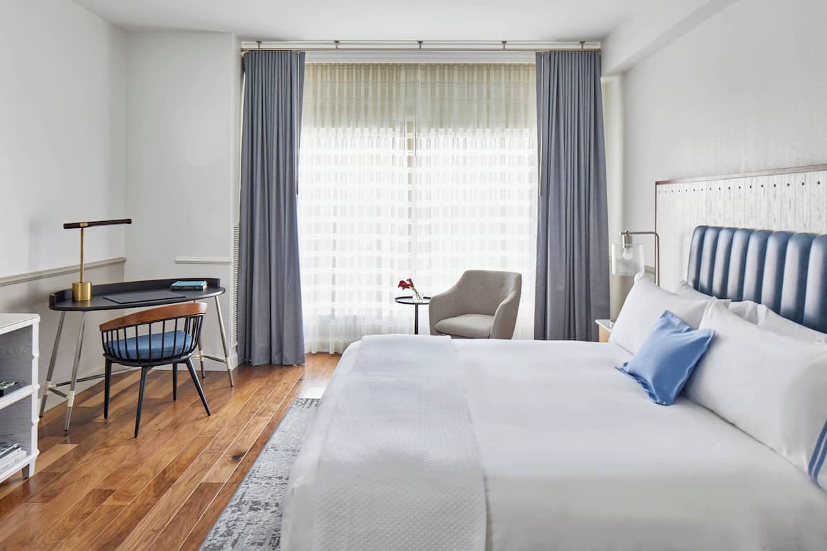 A hotel room with a large bed, a desk, a chair, and a small table.