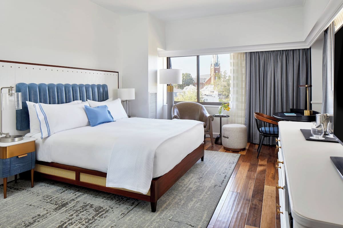 A hotel room with a large bed, a desk, a chair, and a view of the city through the window.