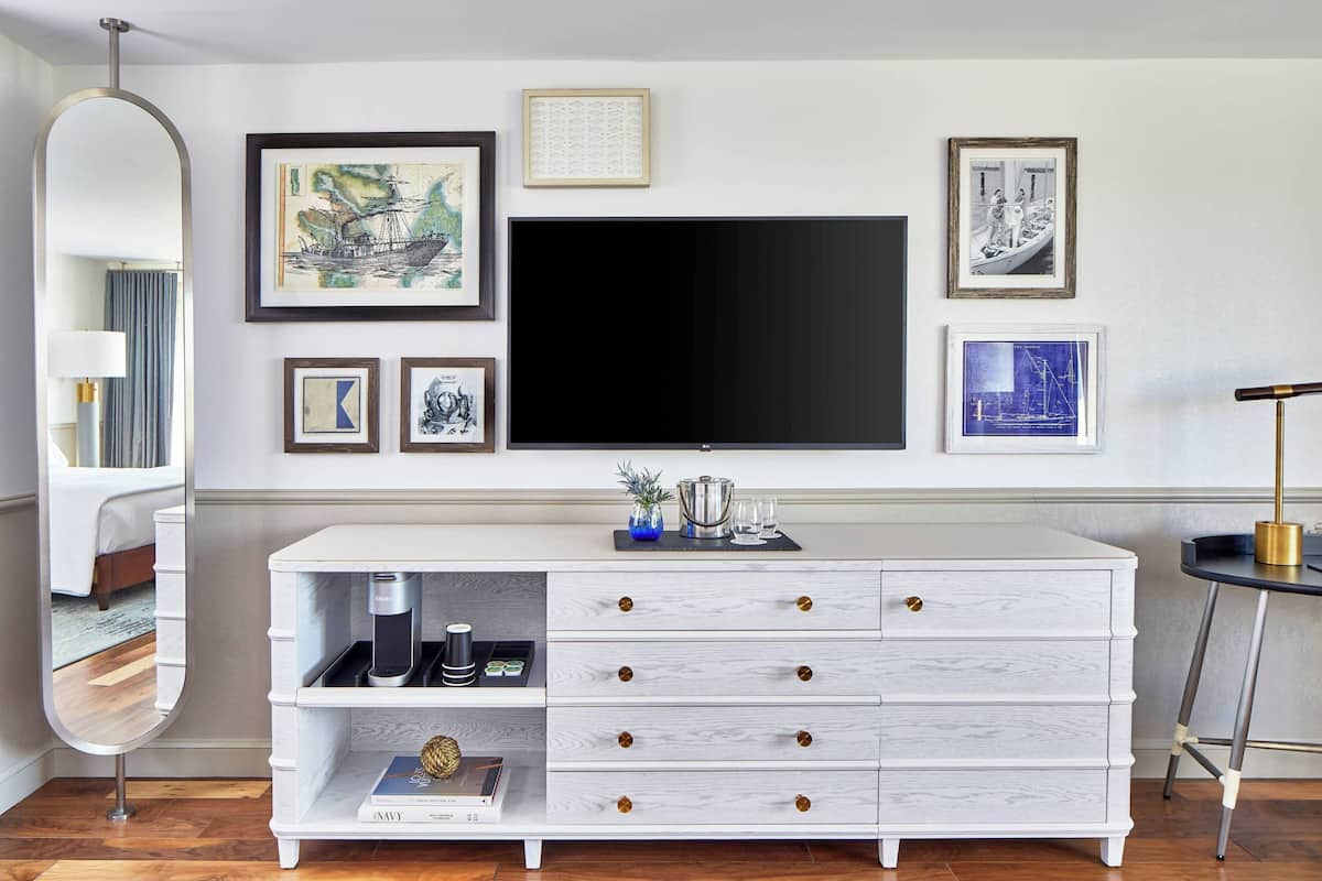 A modern living room with a large flat-screen TV mounted on the wall, a white console table with drawers, and several framed artworks.