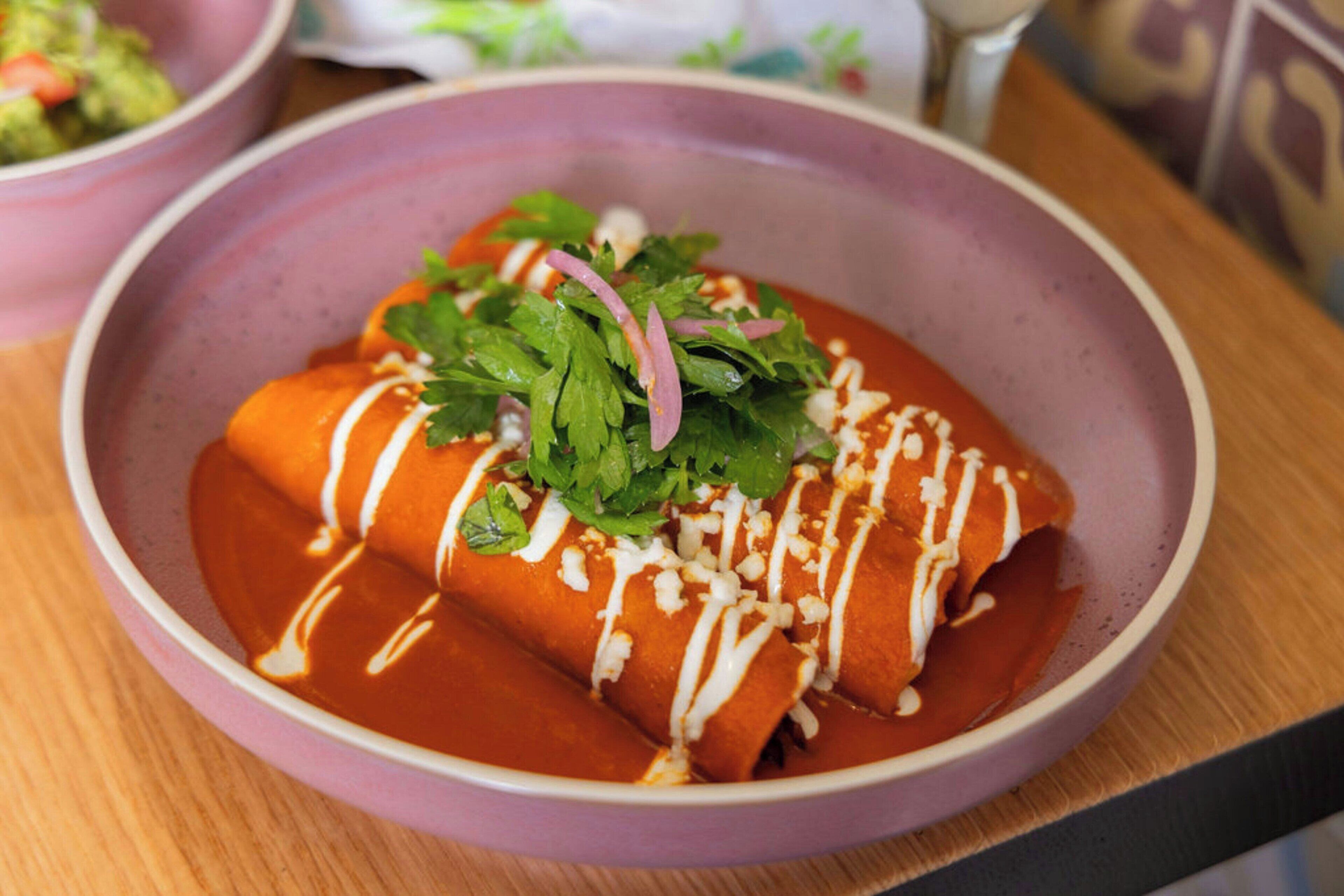 Une assiette d’enchiladas nappées de sauce, recouvertes de fromage et garnies.