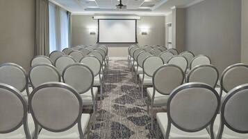 A conference room with rows of chairs, a carpeted floor, a projector screen, and a ceiling-mounted projector.