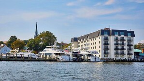 A waterfront property with a docked boat, a tall building with balconies, and a church spire in the background. - Annapolis Waterfront Hotel, Autograph Collection (Annapolis)