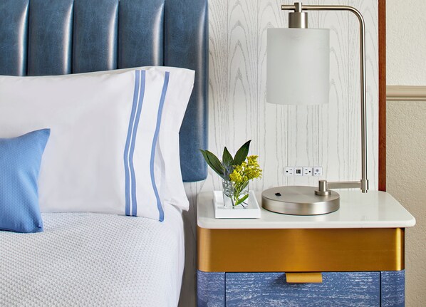 A neatly arranged bedroom with a bed, bedside table, lamp, and a small vase with flowers.