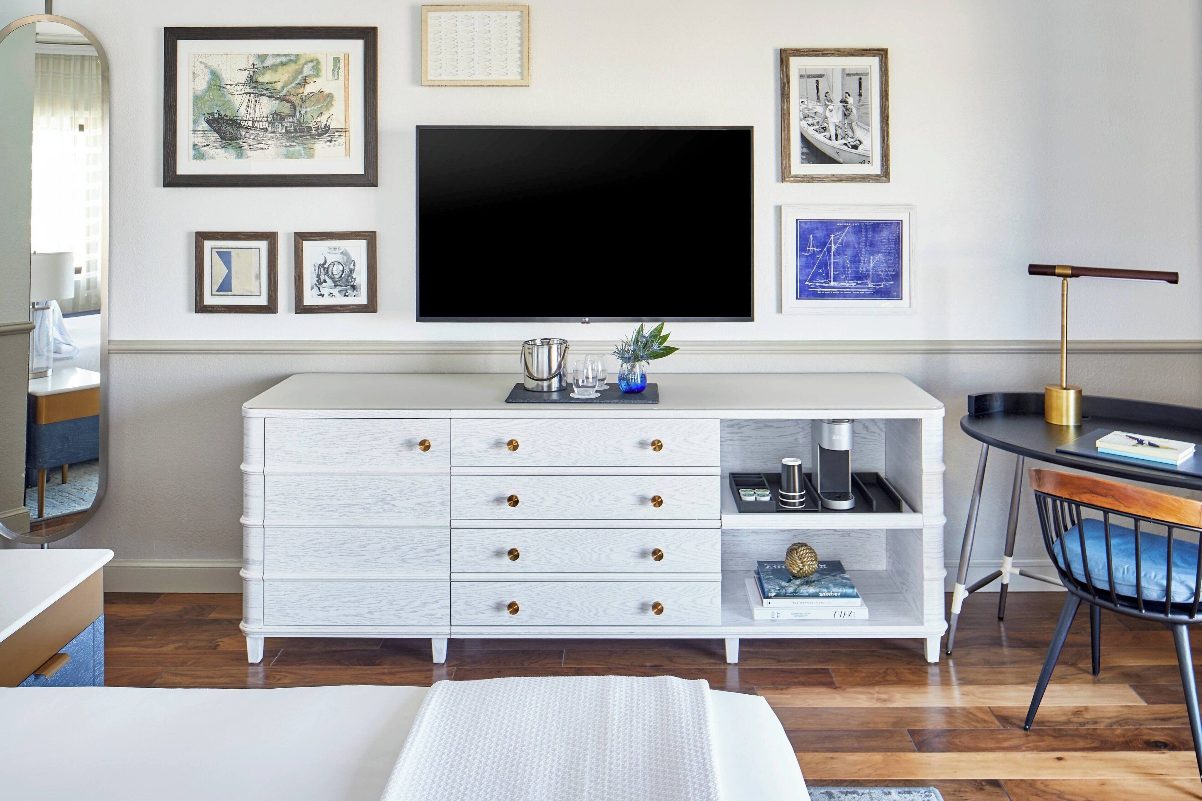 A modern living room with a large flat-screen TV, white cabinetry, and framed artwork on the wall.