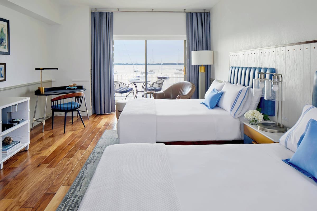 A hotel room with two beds, a desk, a chair, and a view of the sea.