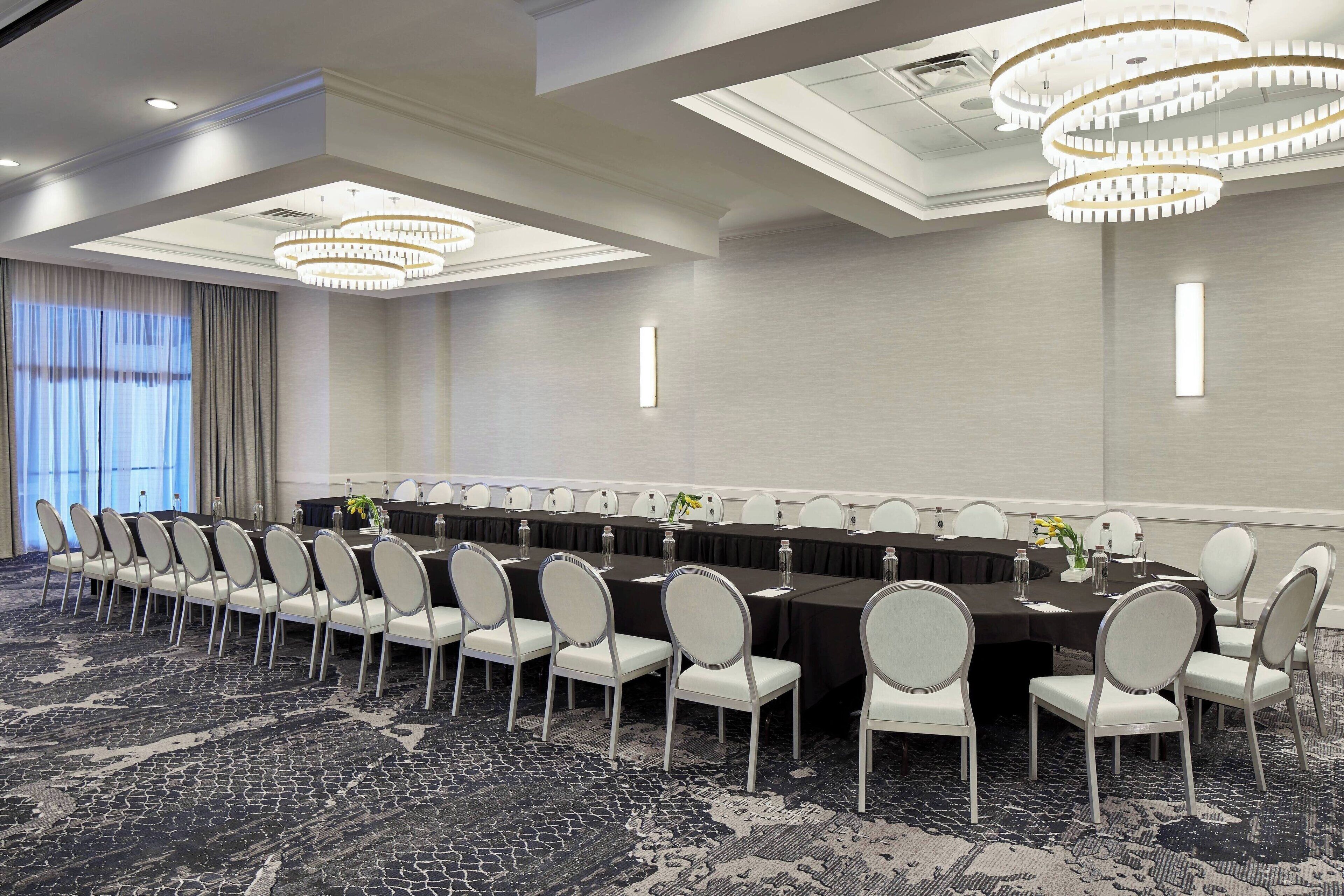 Un salón de conferencias con una larga mesa, sillas blancas y candelabros.