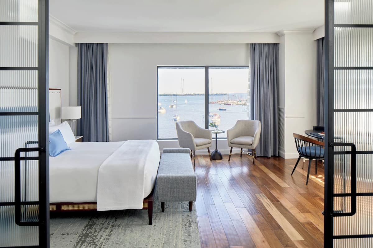 A hotel room with a large bed, two armchairs, a small table, and a view of the sea.