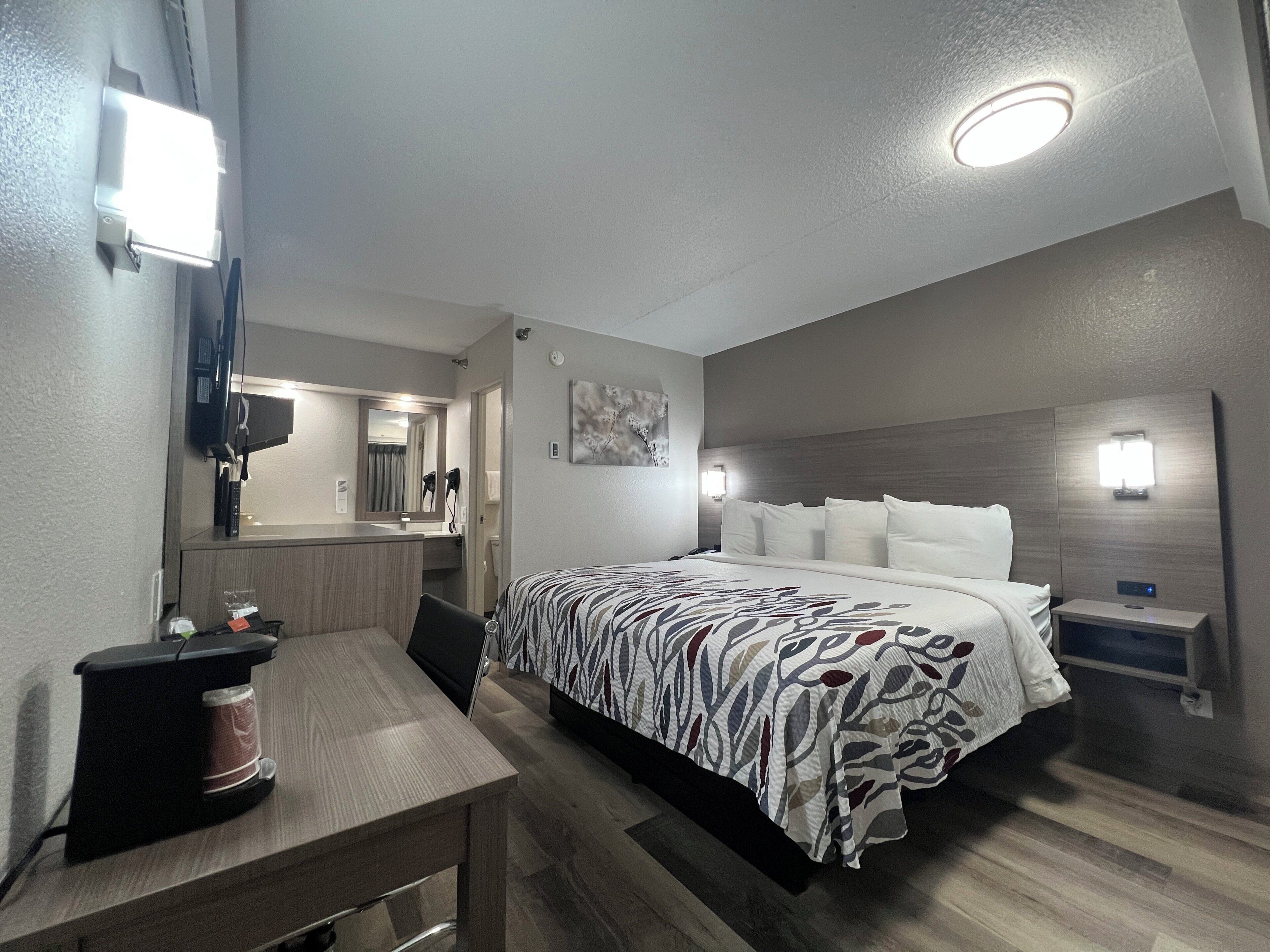 Hotellihuone, jossa on sänky, yöpöytä ja työpöytä sekä kahvinkeitin.