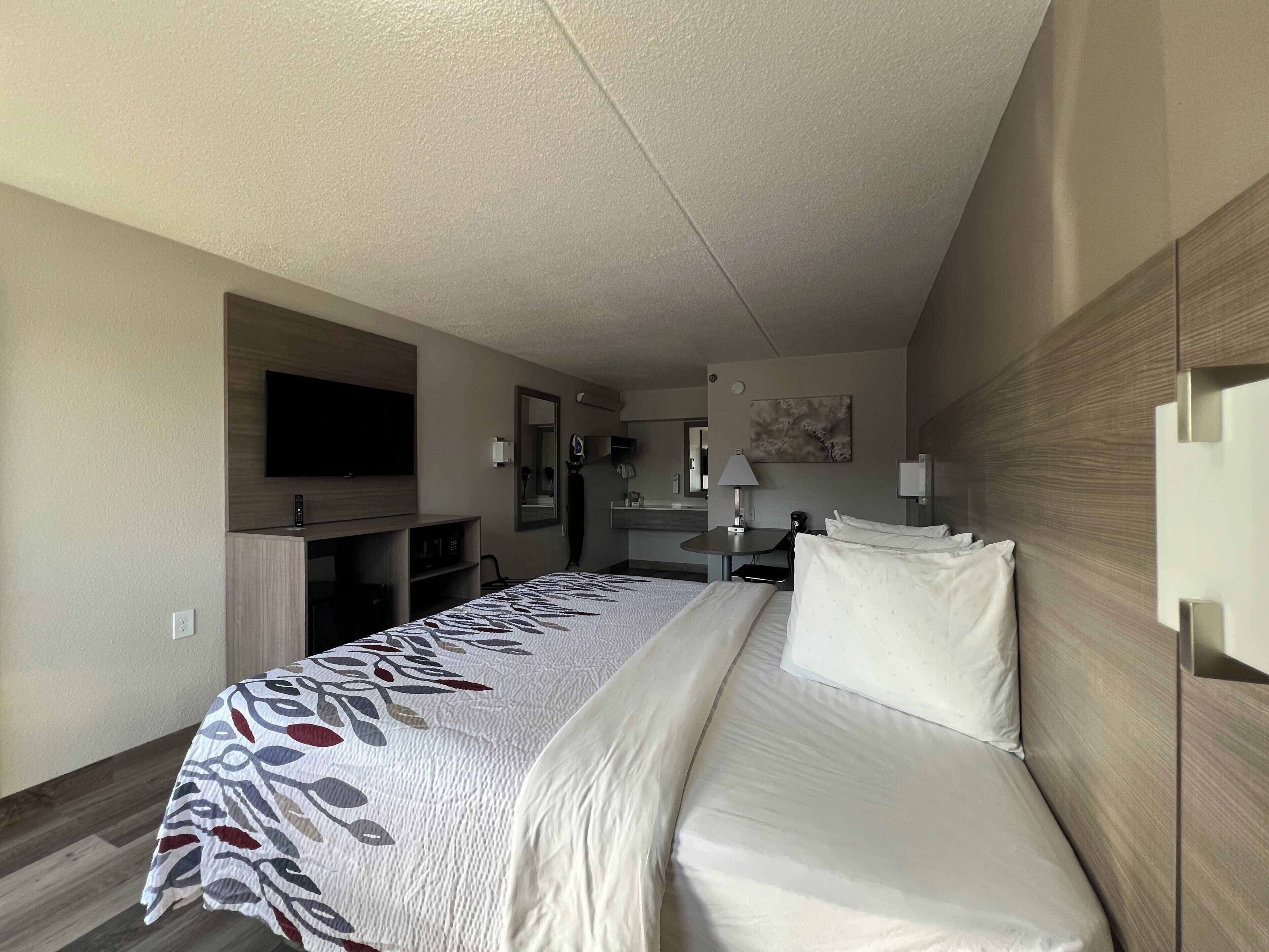 A hotel room with a bed, a TV, a desk, and a mirror.