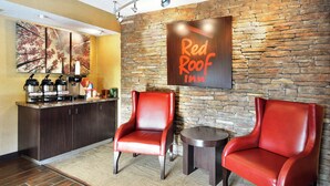A Red Roof Inn reception area with a stone wall, two red leather chairs, a coffee station, and artwork on the wall. - Red Roof Inn Lexington South (Lexington)