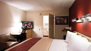 Une chambre d’hôtel comprenant un lit, un bureau avec une télévision, une chaise, une porte et un luminaire fixé au mur.