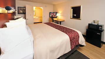 Ein Hotelzimmer mit einem Bett, einem Fernseher, einem Schreibtisch mit einer Lampe und einer Minibar.