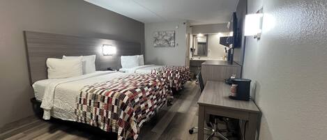 A hotel room with two beds, a desk, a mirror, and a small kitchenette.
