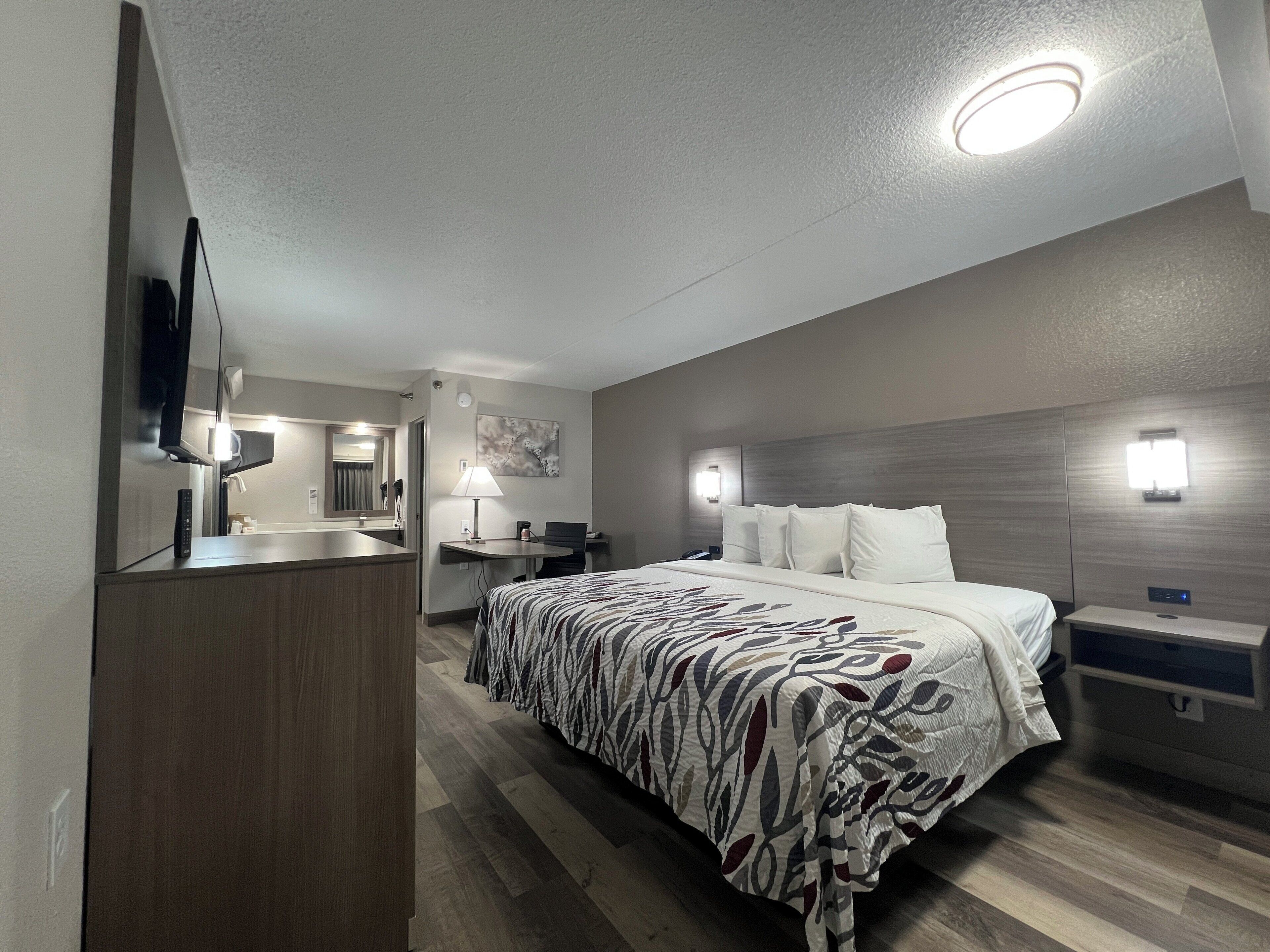 Quarto de hotel moderno com uma cama grande, uma escrivaninha, um espelho e uma televisão.