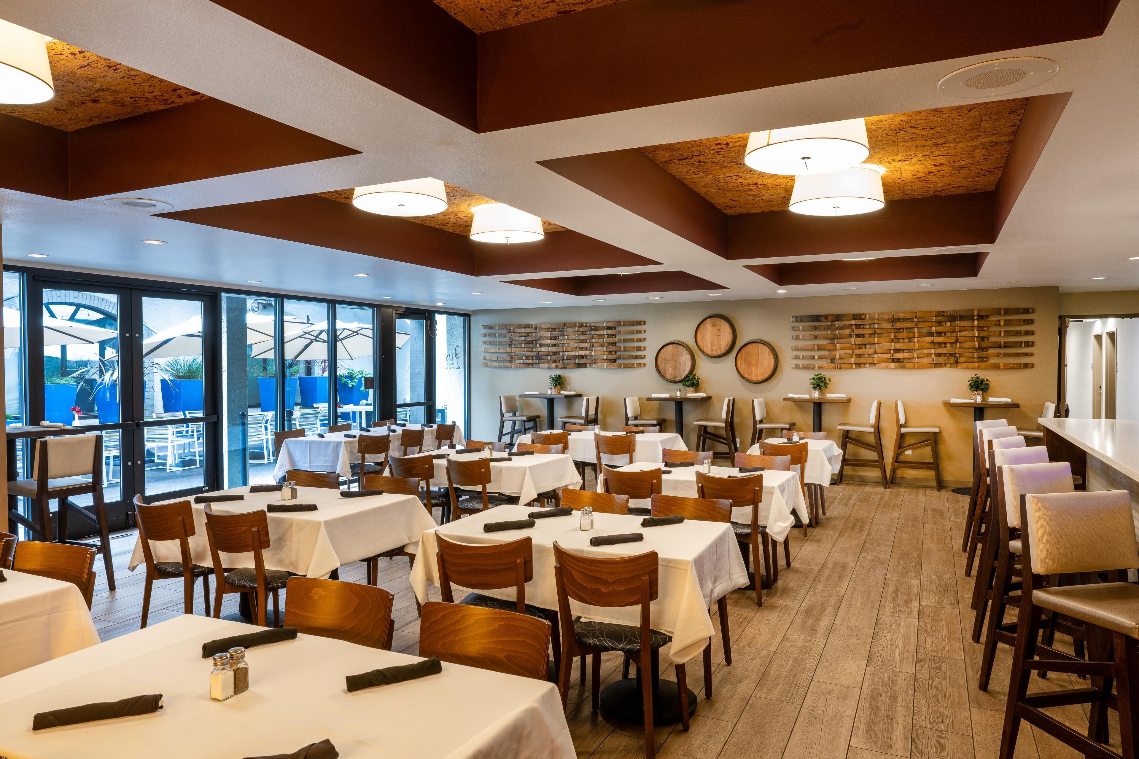 A restaurant with multiple tables and chairs, large windows, and a wooden ceiling.