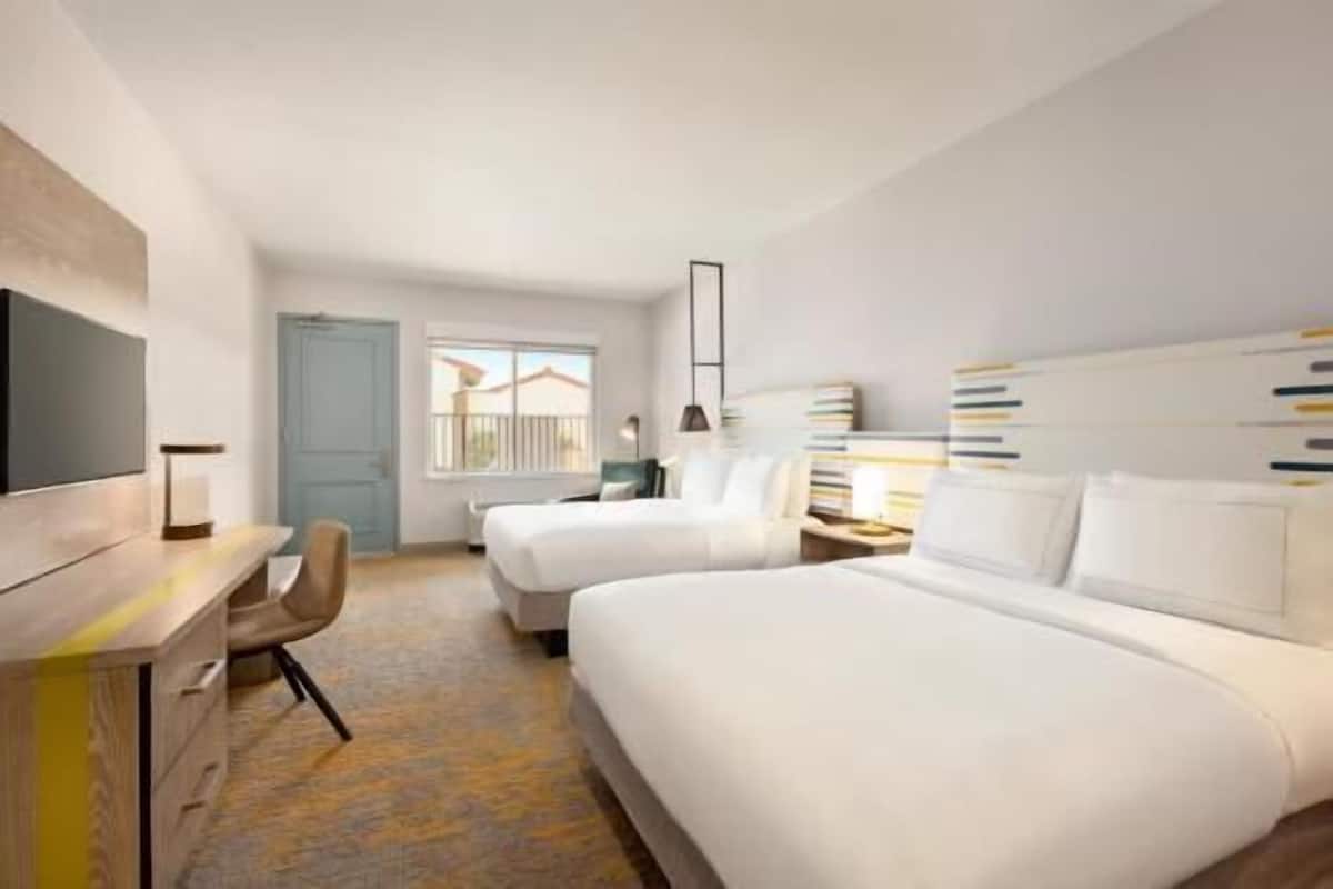Habitación de hotel con dos camas, un escritorio, una silla, un televisor y una ventana con vistas.