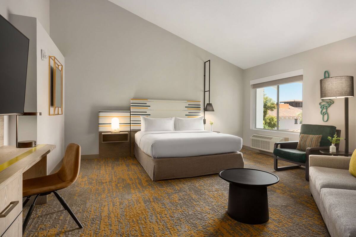 Quarto de hotel moderno com uma cama grande, uma escrivaninha, uma cadeira, um sofá e uma janela com vista.