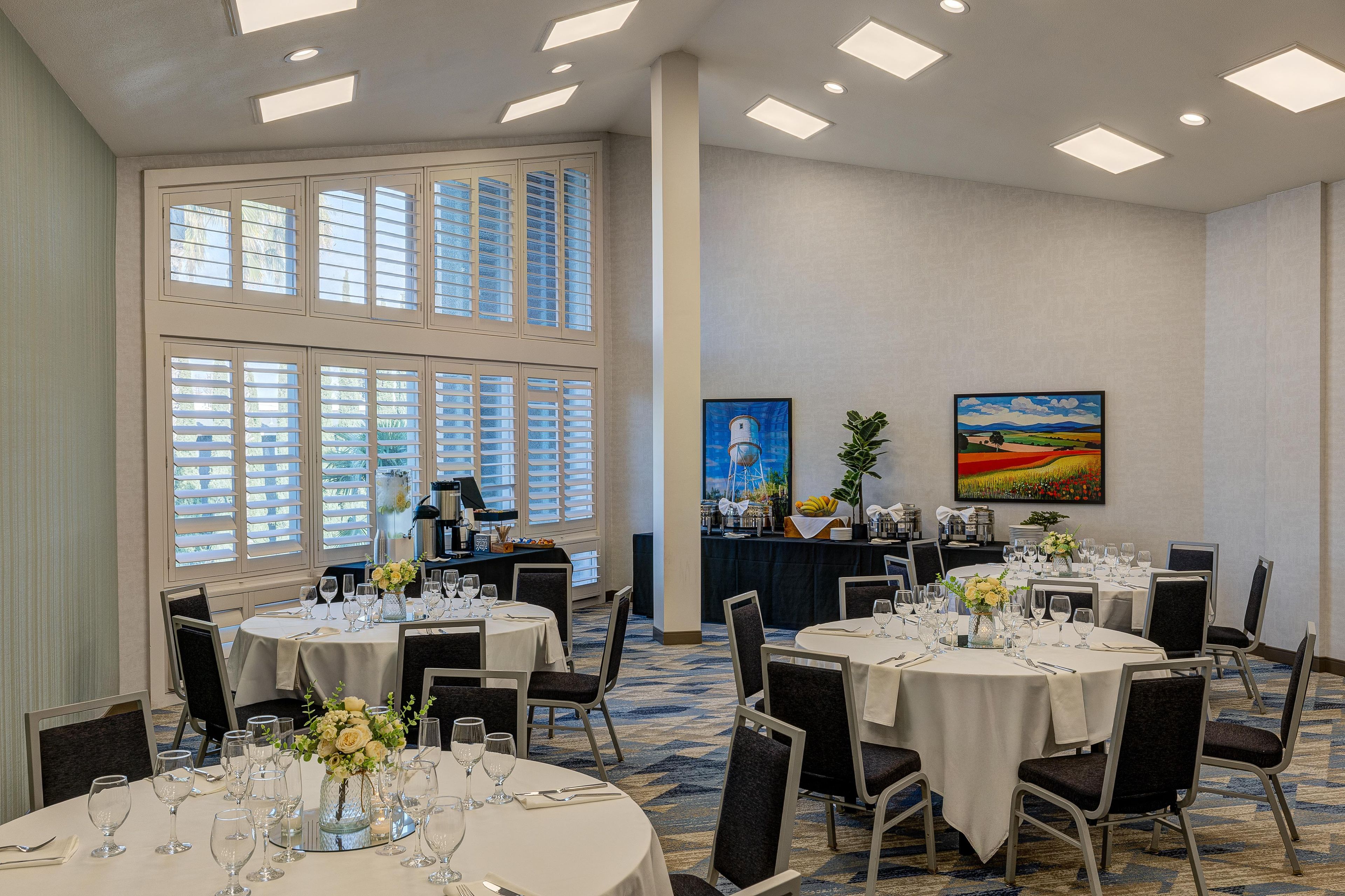 A conference room with round tables, chairs, and a large window with blinds.